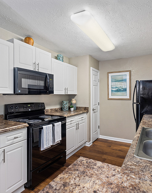 Spacious kitchen with white cabinets, upgraded appliances, granite countertops on wood floors at MAA Berkeley Lake luxury apartments in Duluth, GA