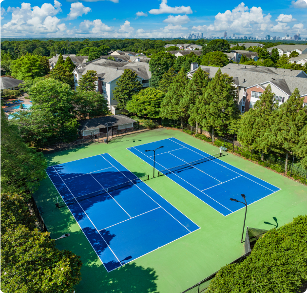Aerial view of two gated tennis courts with lights surrounded by trees at MAA Briarcliff luxury apartments in Atlanta, GA
