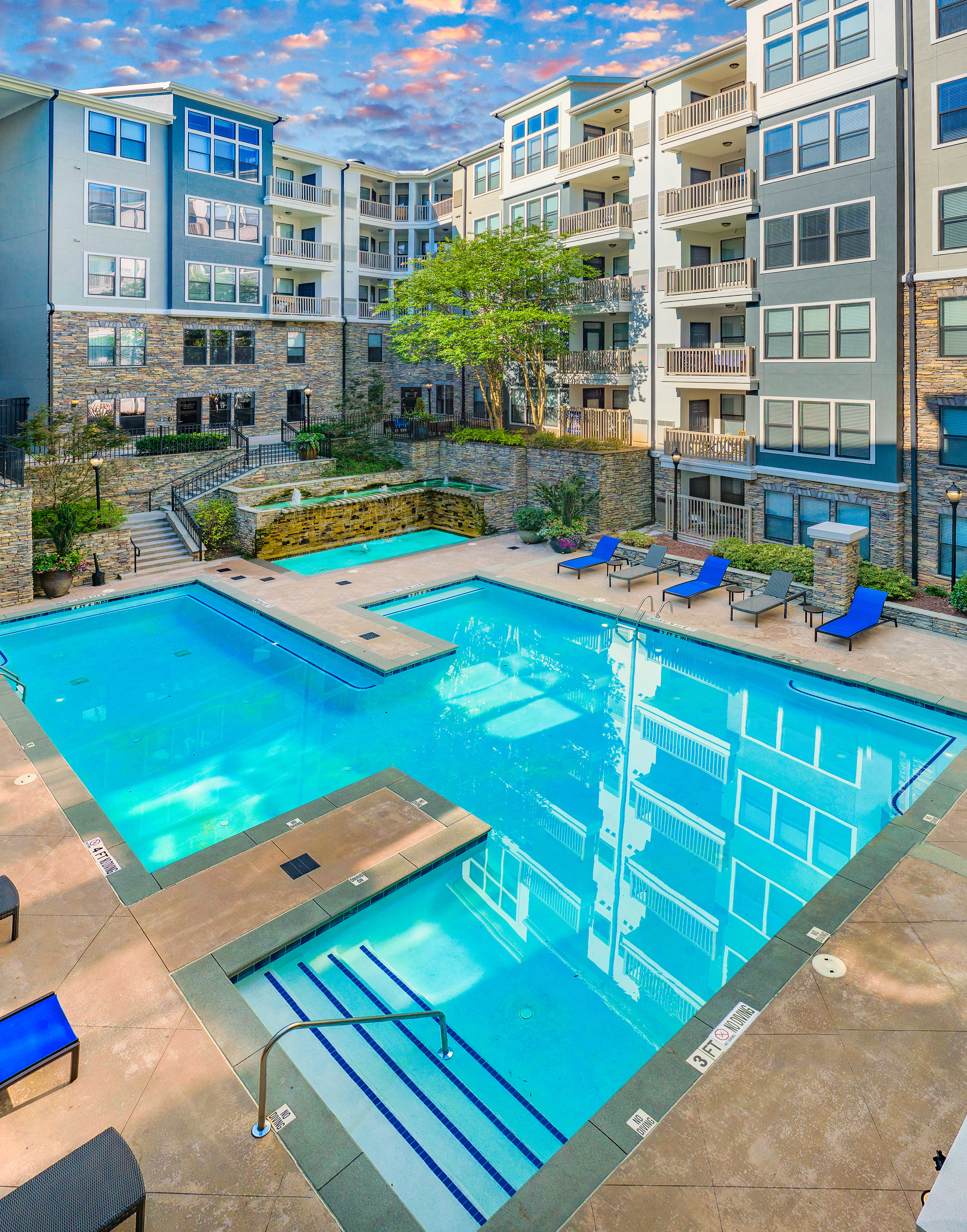 Sectional swimming pool with metal handrails and entrance steps surrounded by lounge chairs and water fountain in the center of the apartment complex at MAA Brookwood luxury apartments in Atlanta, GA