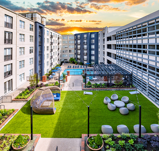 Community outdoor open grassy lounge area with multiple sitting areas, market lights and planters next to outdoor grilling area and pool at MAA Buckhead luxury apartments complex in Atlanta, GA