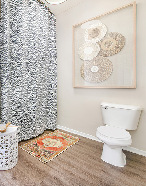Modern bathroom with rustic wall art next to patterned shower curtains and a bathroom mat on wood floors at MAA Buckhead luxury apartments complex in Atlanta, GA