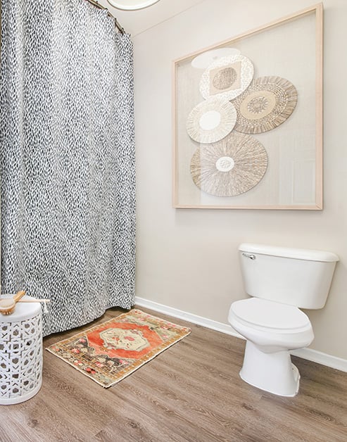 Modern bathroom with rustic wall art next to patterned shower curtains and a bathroom mat on wood floors at MAA Buckhead luxury apartments complex in Atlanta, GA