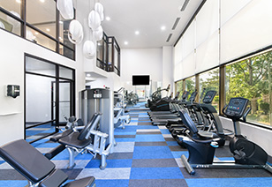 Side view of two-story fitness center with row of treadmills and other workout equipment next to large picture windows and blue carpeted floors at MAA Buckhead luxury apartments complex in Atlanta, GA