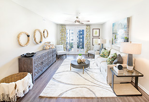 Long view of modern living room with wooden side table and wall art, circular coffee table on white area rug on wood floors at MAA Buckhead luxury apartments complex in Atlanta, GA