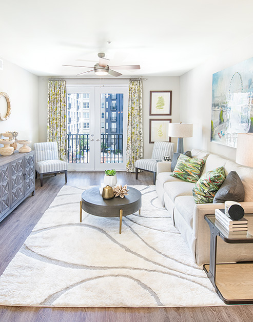 Upscale living room space with white couch, circular coffee table on a white area rug next to glass doors with balcony view on wood floors at MAA Buckhead luxury apartments complex in Atlanta, GA