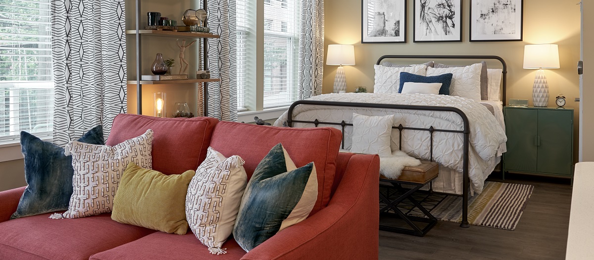 Cozy studio model unit with a bed and red sofa at MAA Centennial Park luxury apartments in Atlanta, GA