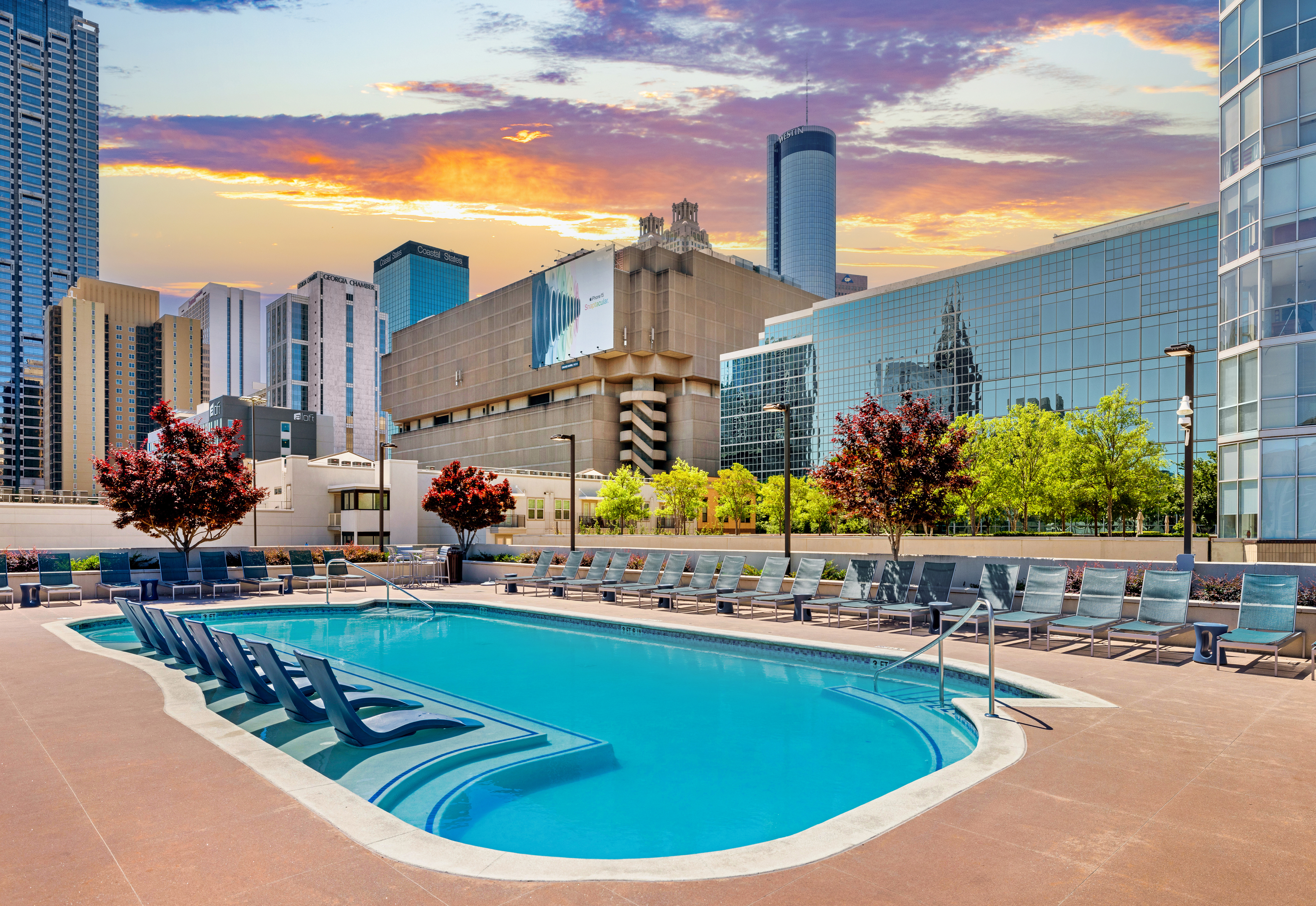 Wide view of rooftop pool with sundeck surrounded by lounge chairs and city buildings with a sunset sky at MAA Centennial Park luxury apartments in Atlanta, GA