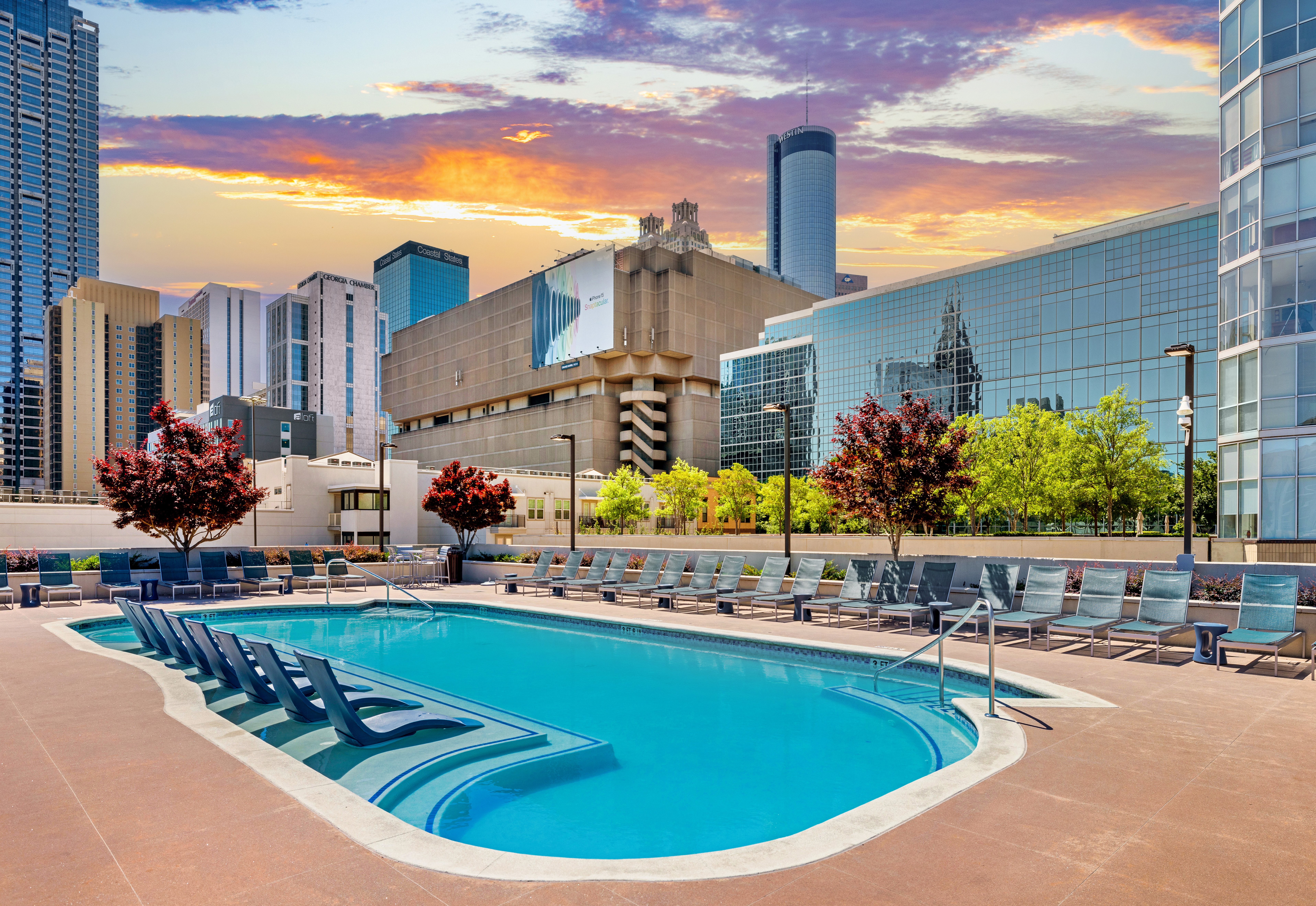 Wide view of rooftop pool with sundeck surrounded by lounge chairs and city buildings with a sunset sky at MAA Centennial Park luxury apartments in Atlanta, GA