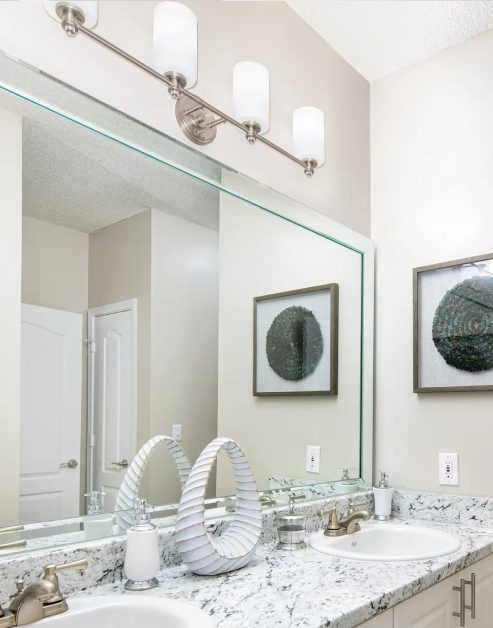 Modern-style bathroom with bright lighting above large vanity mirror and double sinks at MAA Gardens luxury apartments in Atlanta, GA