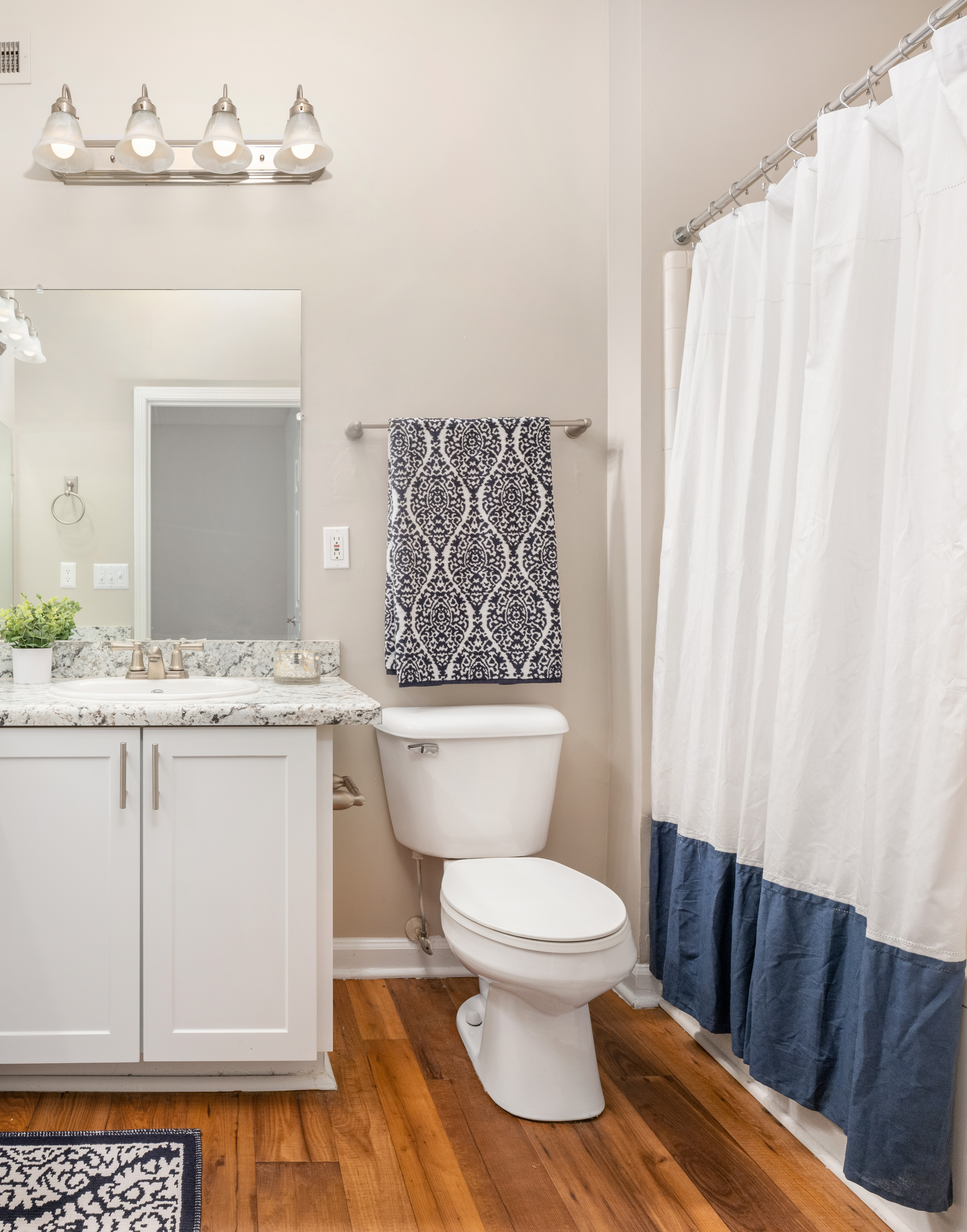 Model bathroom with a single vanity and sink on light-colored countertops, white cabinets next to a toilet and white shower curtains on wood floors at MAA Lake Lanier luxury apartments in Gainesville, GA