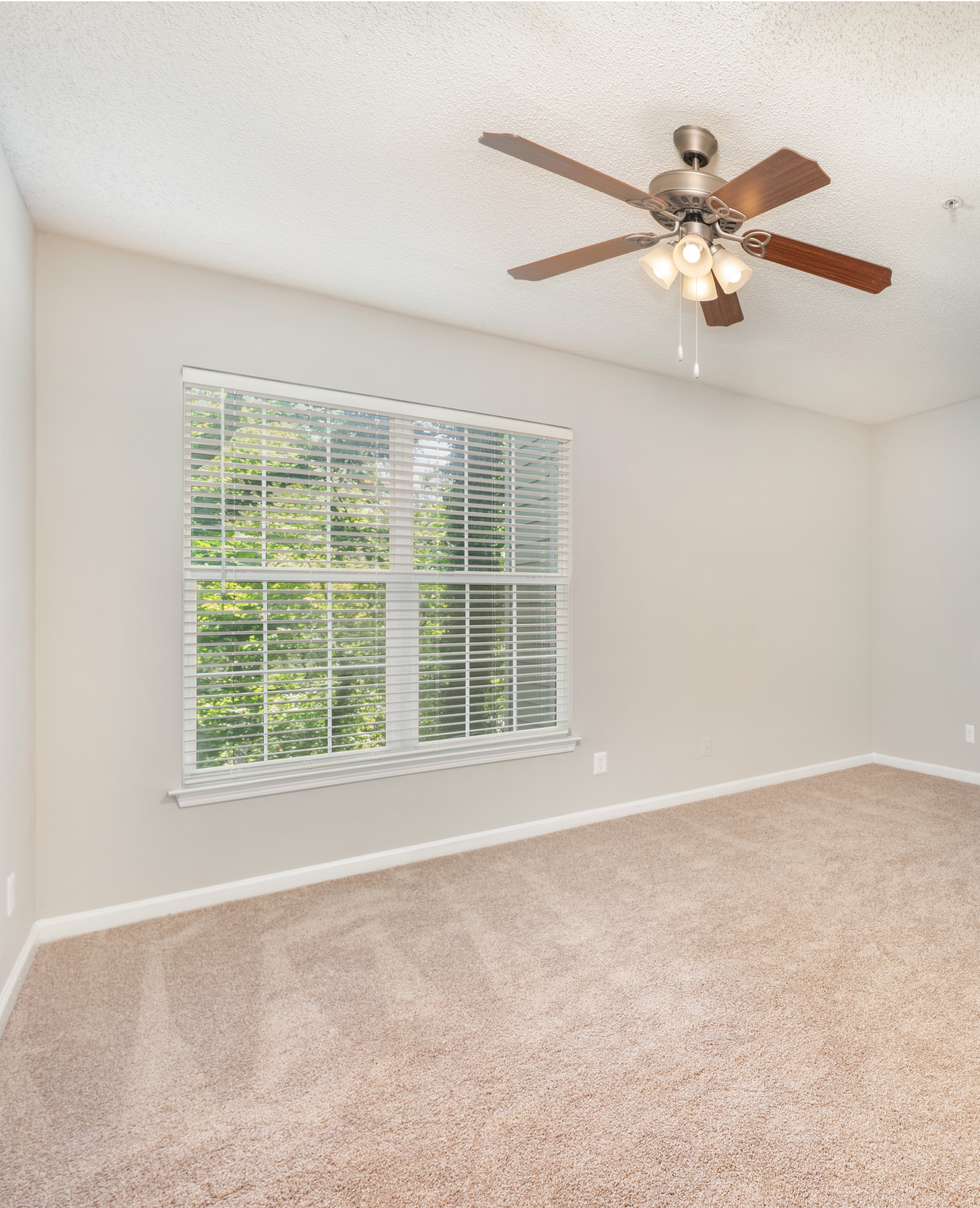 Empty carpeted bedroom with a ceiling fan and large picture window with blinds at MAA Lake Lanier luxury apartments in Gainesville, GA