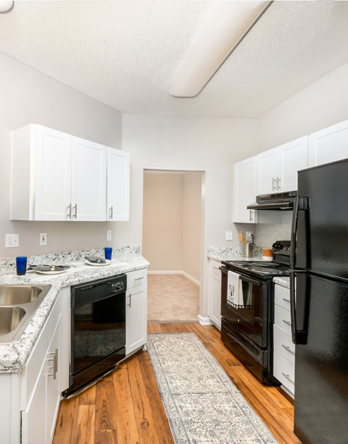 Model kitchen with grey and white marble countertops, white cabinets, and upgraded appliances on wood floors with a runner rug at MAA Lake Lanier luxury apartments in Gainesville, GA