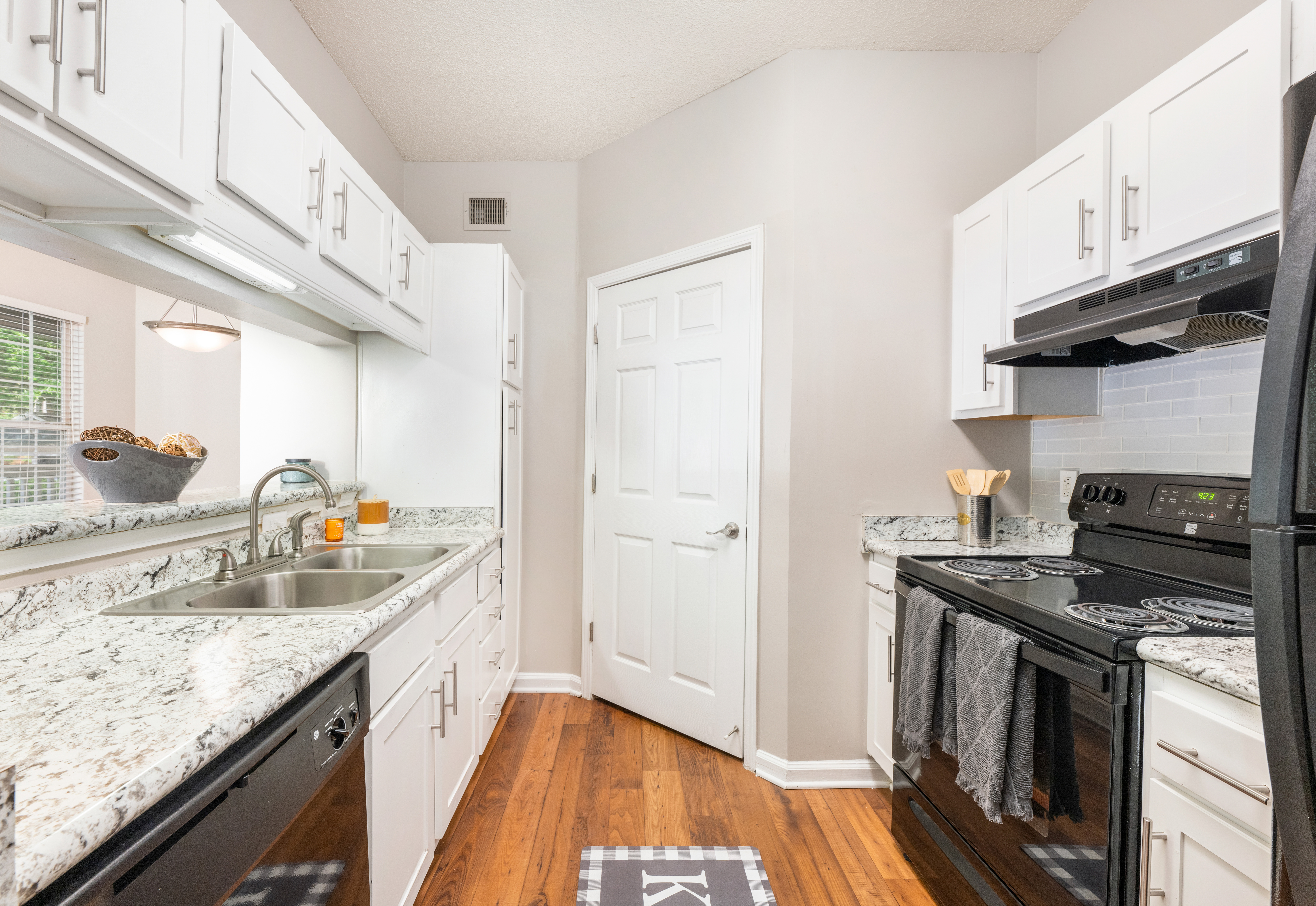 Side view of kitchen with grey and white marble countertops, white cabinets, and upgraded appliances on wood floors at MAA Lake Lanier luxury apartments in Gainesville, GA