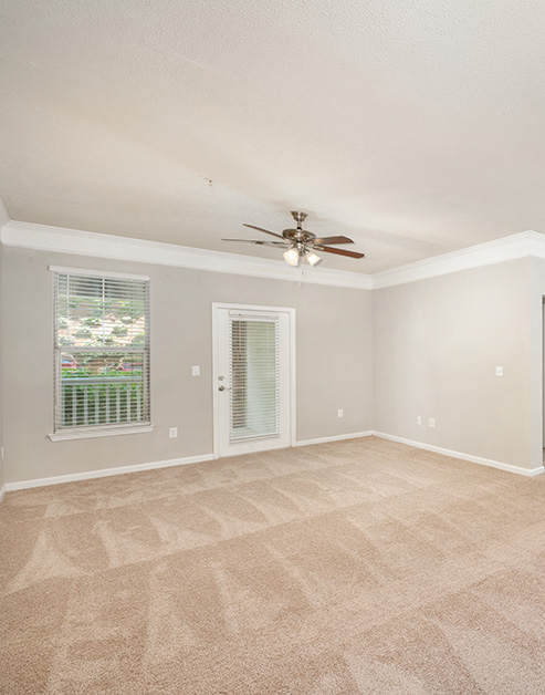 Spacious empty carpeted living room area with a ceiling fan, glass side door to the balcony with a window at MAA Lake Lanier luxury apartments in Gainesville, GA