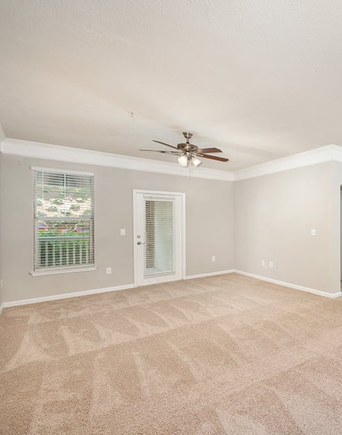 Spacious empty carpeted living room area with a ceiling fan, glass side door to the balcony with a window at MAA Lake Lanier luxury apartments in Gainesville, GA