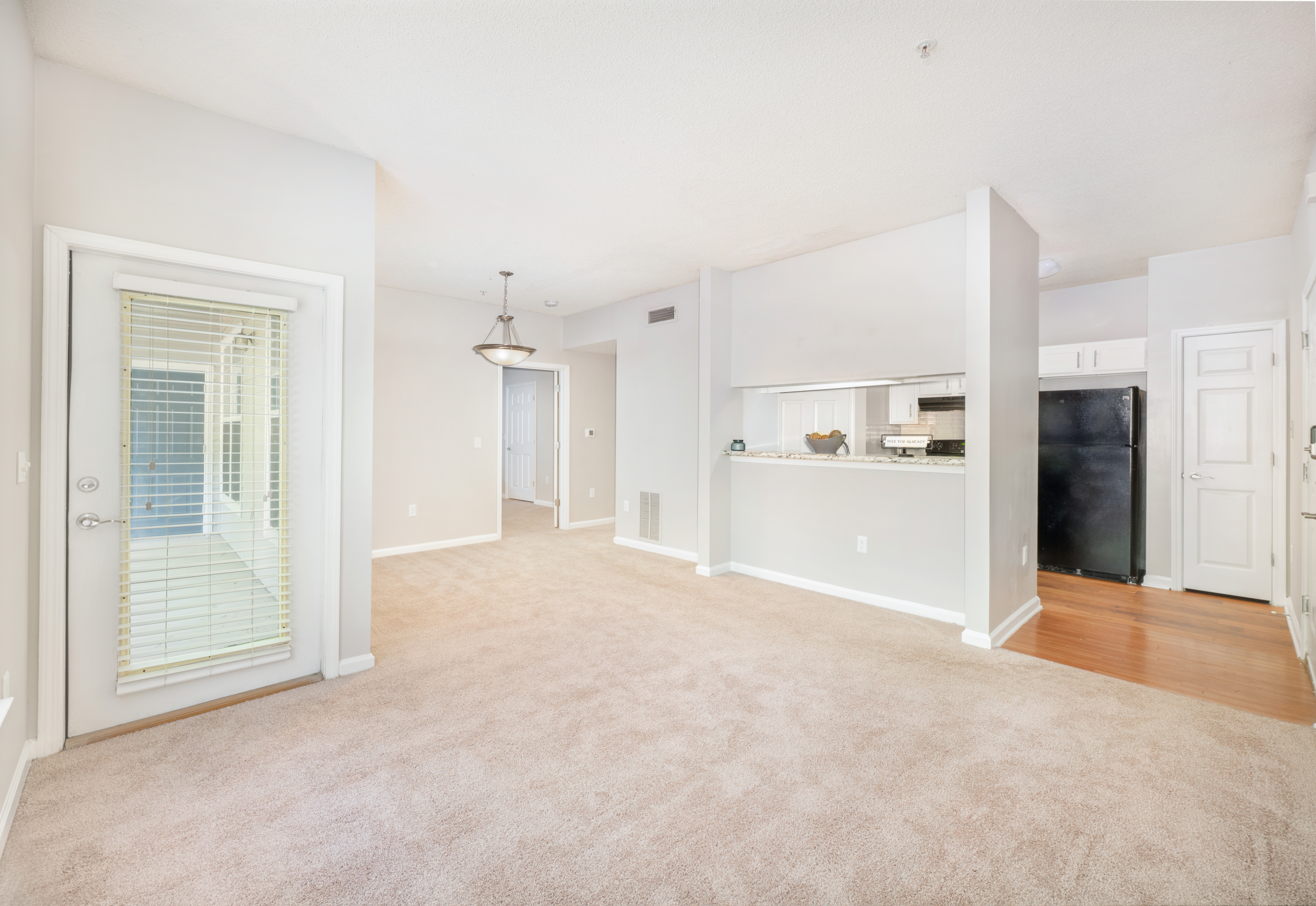 Long view of spacious empty carpeted living room with a ceiling fan next to a kitchen with wood floors at MAA Lake Lanier luxury apartments in Gainesville, GA