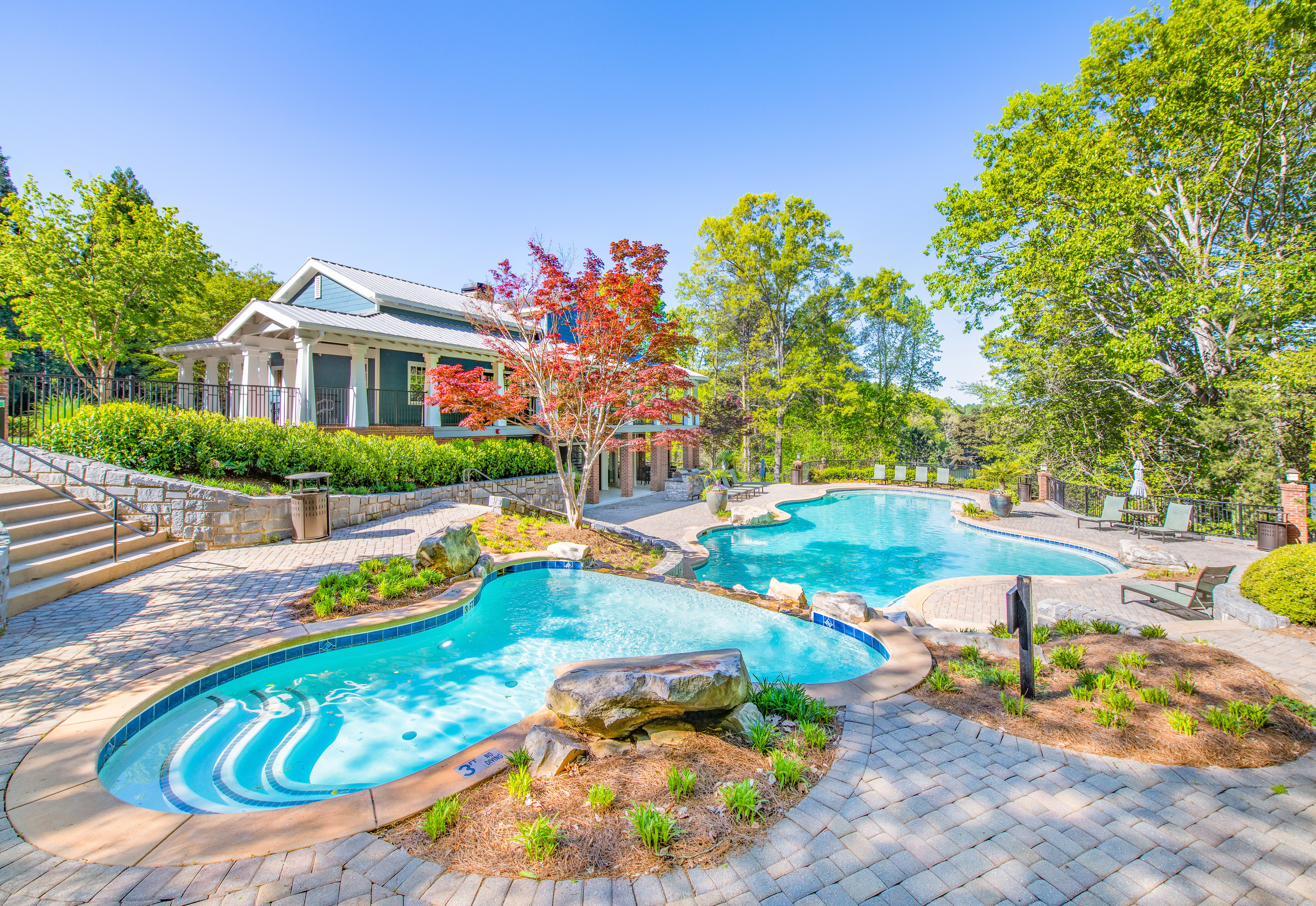 Long view of a double wading pool in the shade surrounded by planters and trees at MAA Lake Lanier luxury apartments in Gainesville, GA