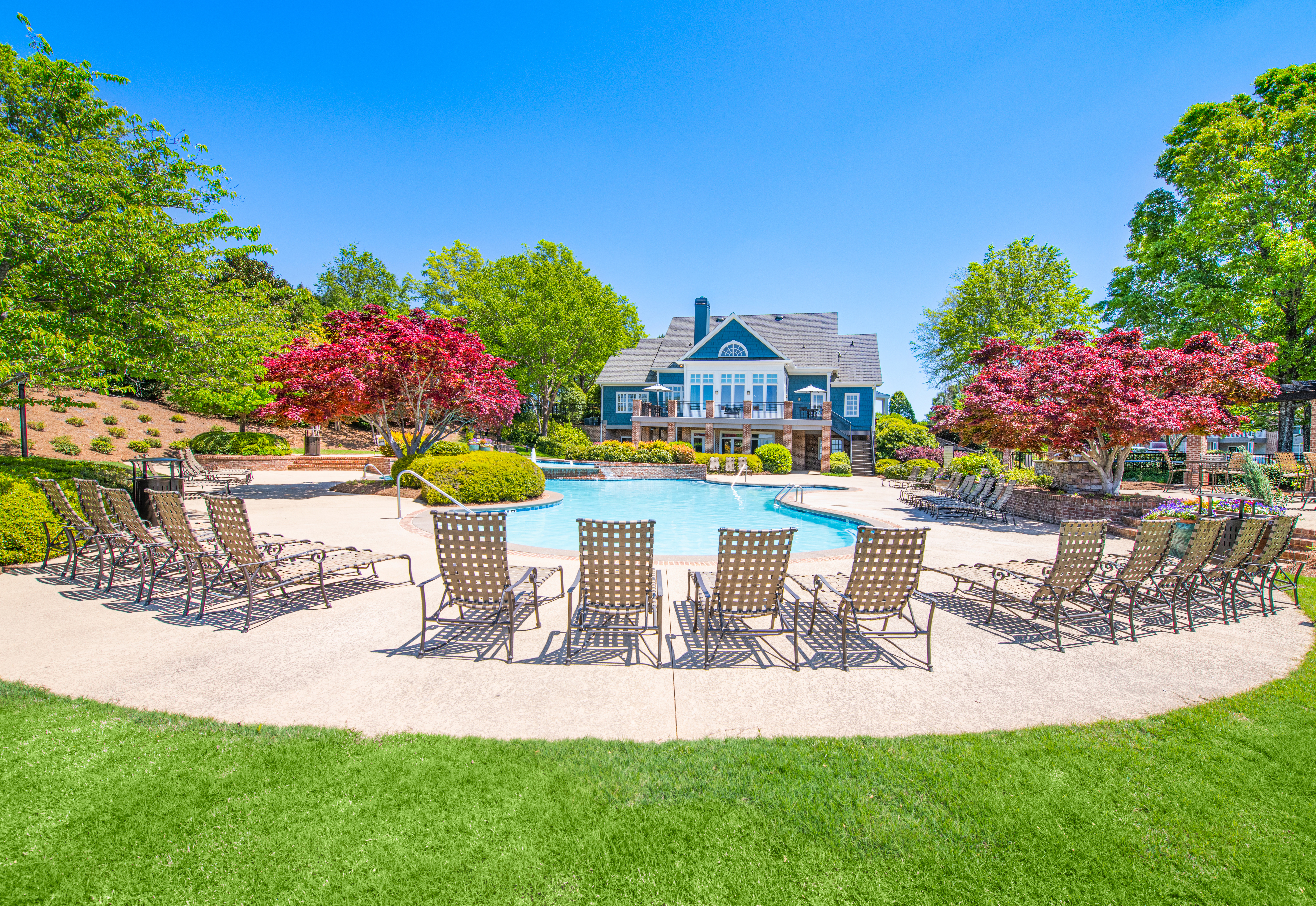 Side view of swimming pool with lounge chairs on the pavement next to a grassy area at MAA Lake Lanier luxury apartments in Gainesville, GA