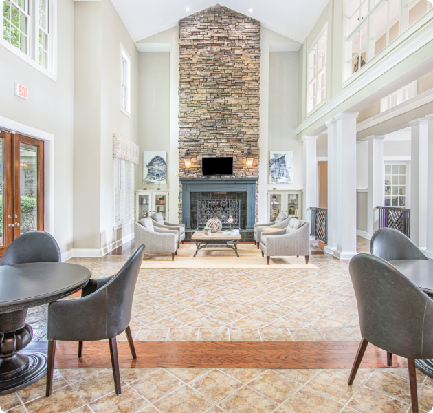 Indoor common area with tables and chairs, a sitting area next to a fireplace and high ceilings at MAA McDaniel Farm luxury apartments in Duluth, GA