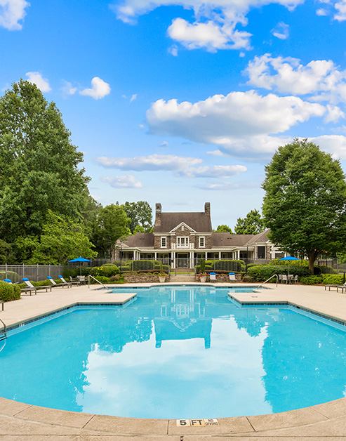 Swimming pool surrounded by lush greenery next to community clubhouse with sunny skies at MAA McDaniel Farm luxury apartments in Duluth, GA