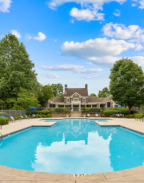 Swimming pool surrounded by lush greenery next to community clubhouse with sunny skies at MAA McDaniel Farm luxury apartments in Duluth, GA