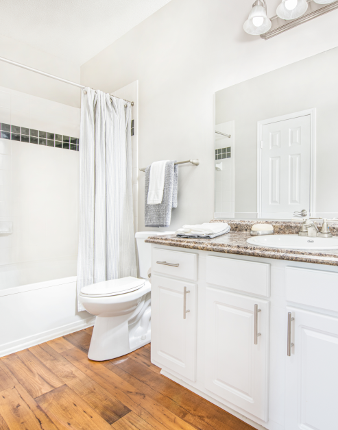 Modern bathroom with a single vanity sink, brown marble countertops and bathtub with white shower curtains at MAA McDaniel Farm luxury apartments in Duluth, GA