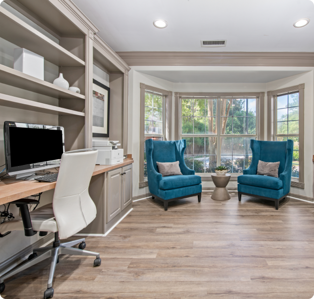 Spacious community workstations next to blue sofa chairs with a bay window view at MAA Milstead luxury apartments in Kennesaw, GA