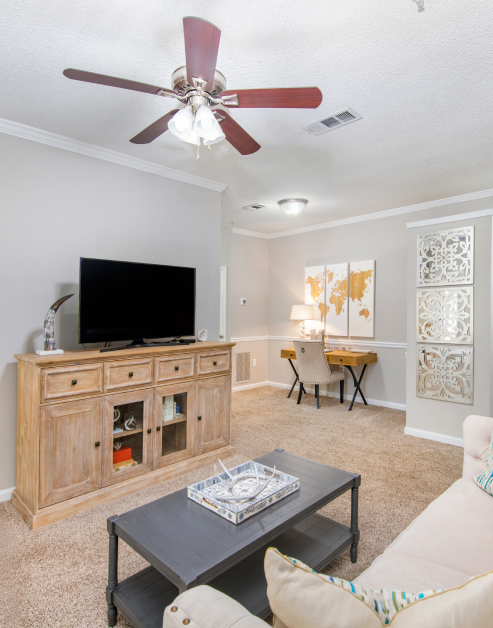 Stylish model living room with rustic brown entertainment center and TV with a ceiling fan at MAA Milstead luxury apartments in Kennesaw, GA