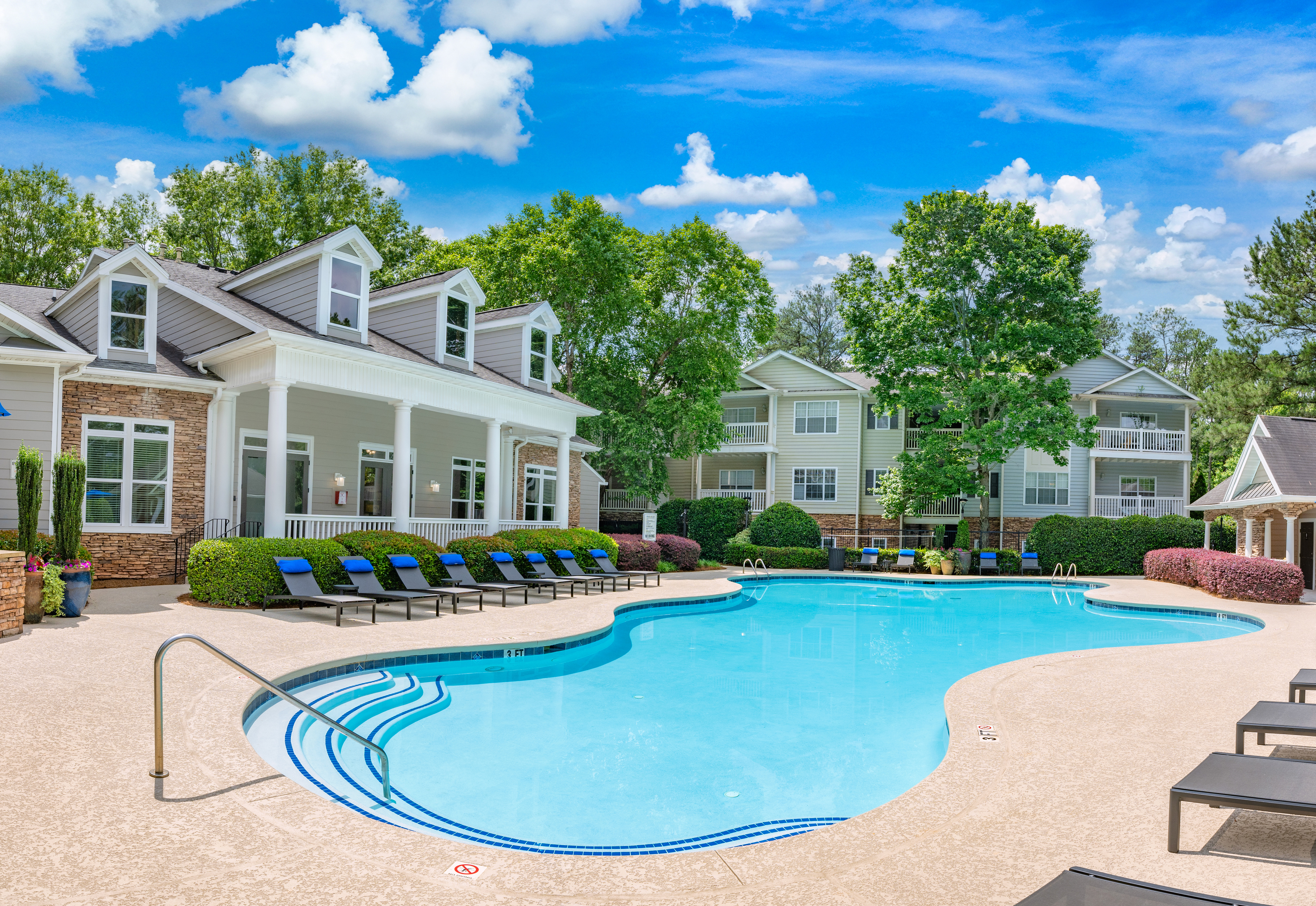 Side view of swimming pool with lounge chairs surrounded by lush greenery next to the clubhouse at MAA Mount Vernon luxury apartments in Sandy Springs, GA