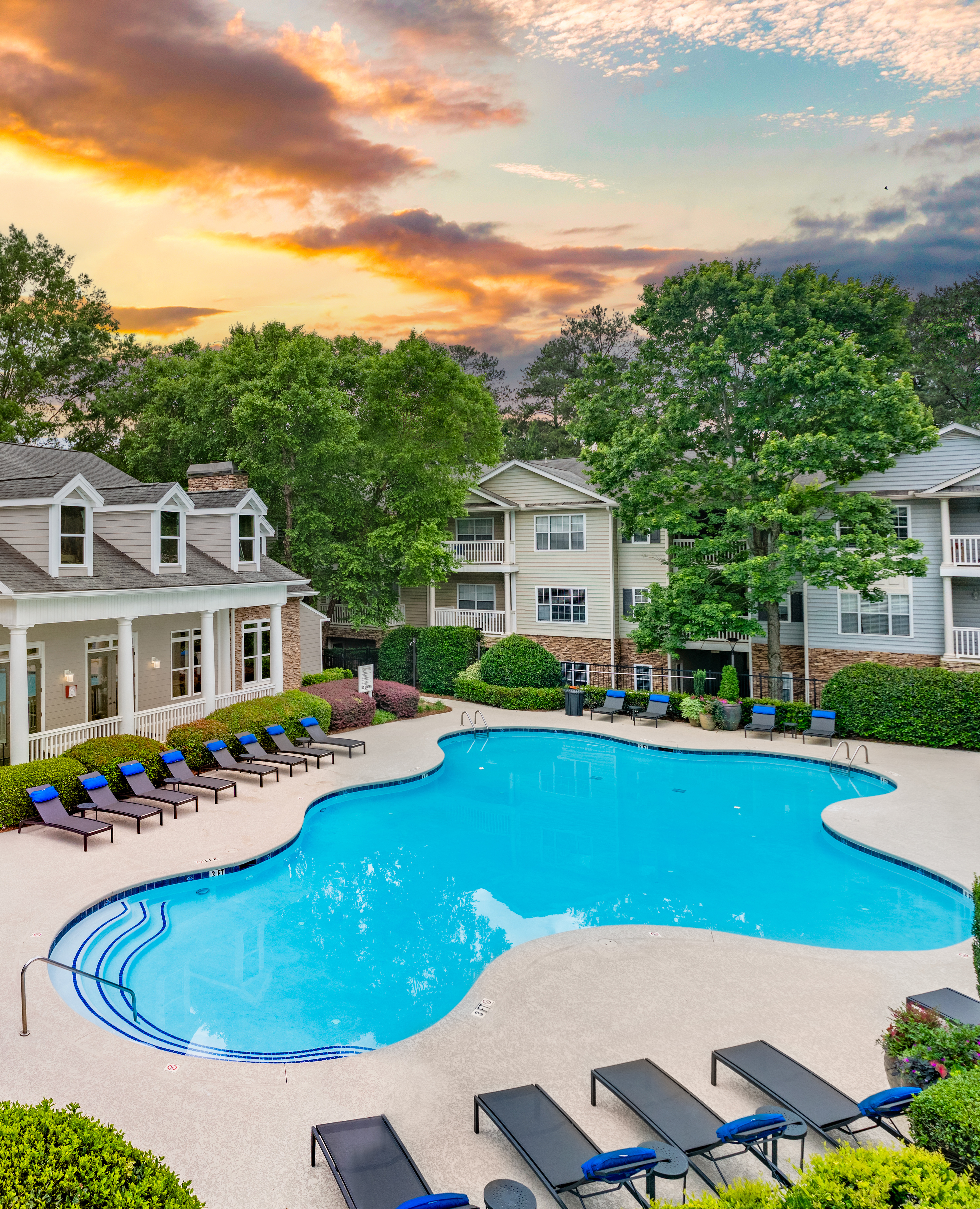 Swimming pool with lounge chairs surrounded by lush greenery next to the clubhouse with a sunset sky at MAA Mount Vernon luxury apartments in Sandy Springs, GA