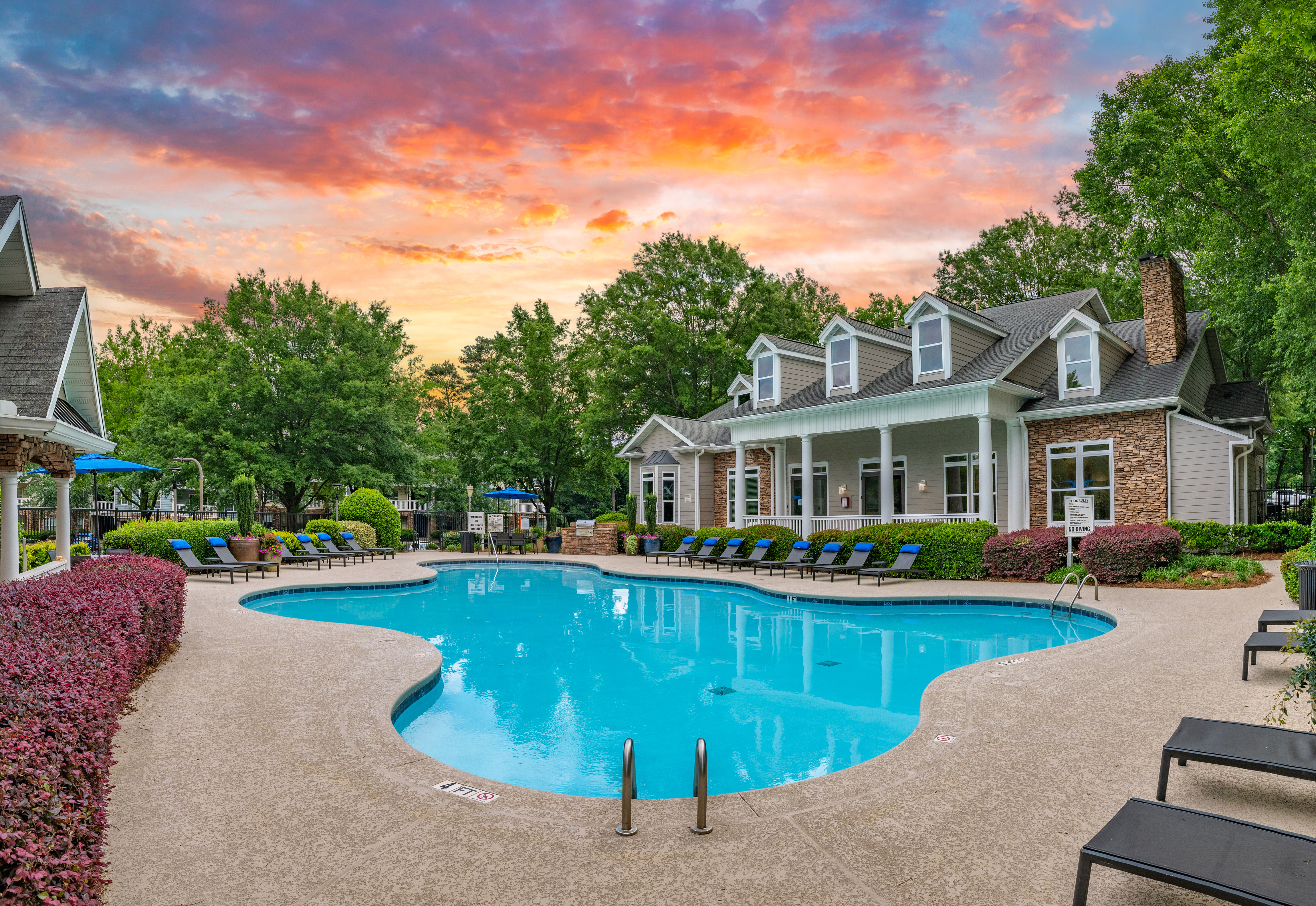 Long view of swimming pool with lounge chairs surrounded by lush greenery next to the clubhouse with a sunset sky at MAA Mount Vernon luxury apartments in Sandy Springs, GA