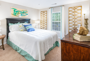 Model guest bedroom with white/green bedding, accent pillows and picture window at MAA Mount Vernon luxury apartments in Sandy Springs, GA