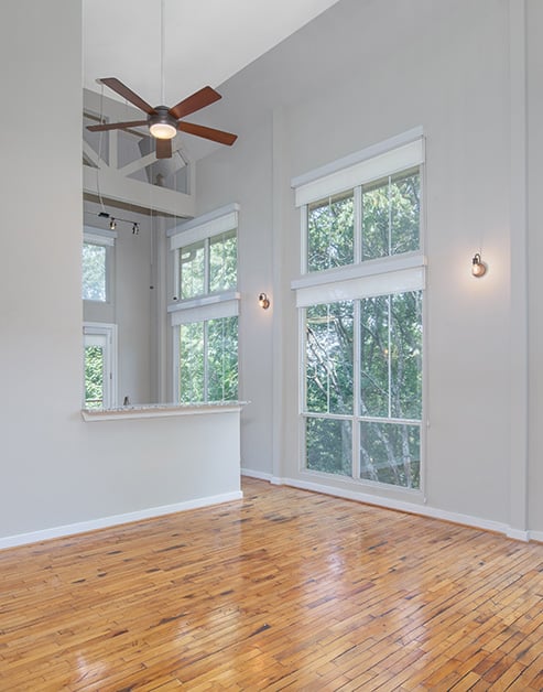 Spacious empty living room with 10-foot ceilings and a ceiling fan, large picture windows on hard wood floors at MAA Piedmont Park luxury apartments in Atlanta, GA