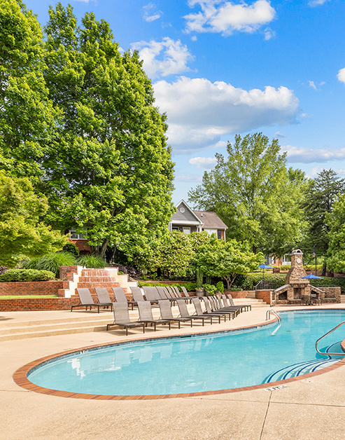 Swimming pool with rows of lounge chairs in front of a tiered waterfall with lush trees at MAA Pleasant Hill luxury apartments in Duluth, GA