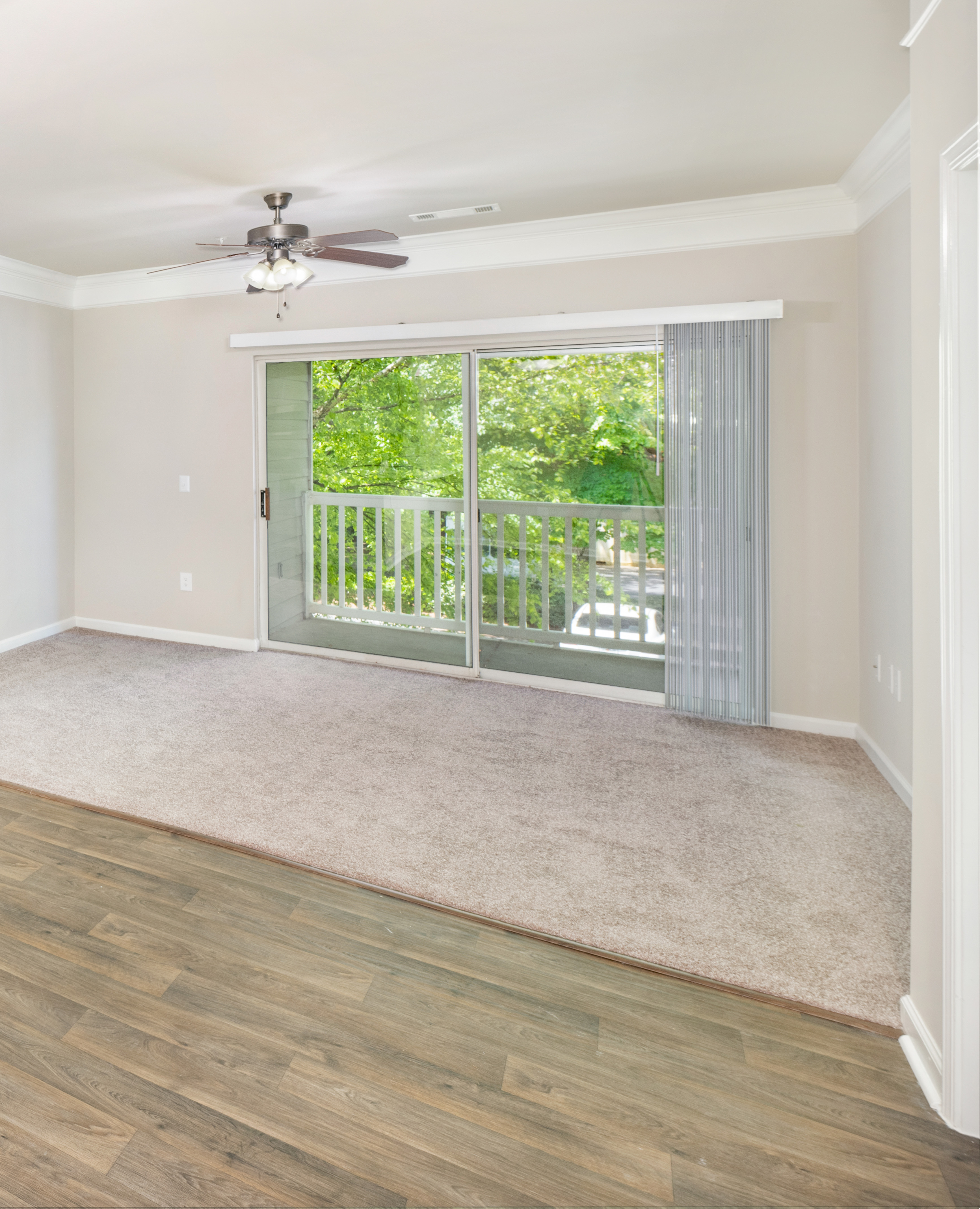 Spacious empty living room with a ceiling fan, large glass sliding doors to a balcony view with half wood and carpet floors at MAA Prescott luxury apartments in Duluth, GA