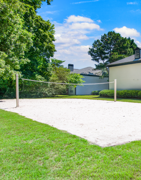 Community outdoor sand volleyball court next to lush trees at MAA River Oaks luxury apartments in Duluth, GA