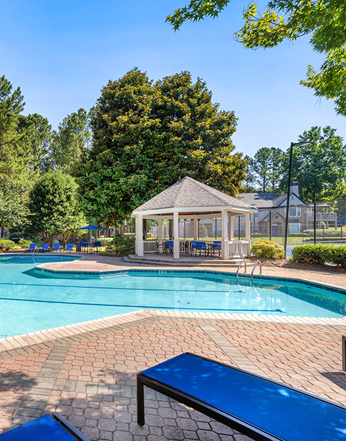 Swimming pool with lush trees and blue lounge chairs next to community gazebo at MAA River Place luxury apartments in Duluth, GA