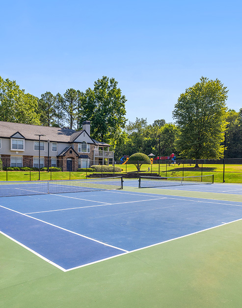 Community tennis courts next to grassy area with large trees at MAA River Place luxury apartments in Duluth, GA