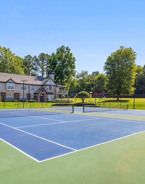 Community tennis courts next to grassy area with large trees at MAA River Place luxury apartments in Duluth, GA