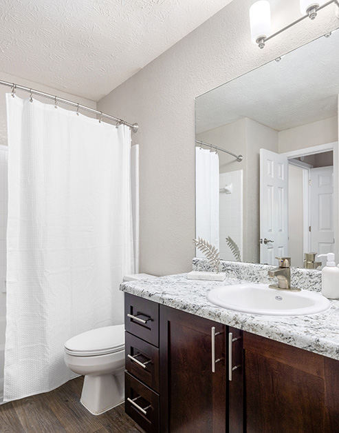 Upscale bathroom with dark wood cabinets, grey countertops with single sink vanity and hard wood floors at MAA River Place luxury apartments in Duluth, GA