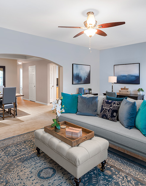 Model living room with arch entryway, a ceiling fan and grey couch with accent pillows next to an off-white ottoman on an area rug at MAA Riverside luxury apartments in Atlanta, GA