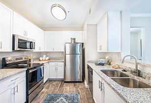 Side view of kitchen with dome ceiling light, white cabinets, stainless steel appliances and granite countertops on wood floors at MAA Riverside luxury apartments in Atlanta, GA