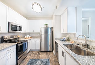 Side view of kitchen with dome ceiling light, white cabinets, stainless steel appliances and granite countertops on wood floors at MAA Riverside luxury apartments in Atlanta, GA