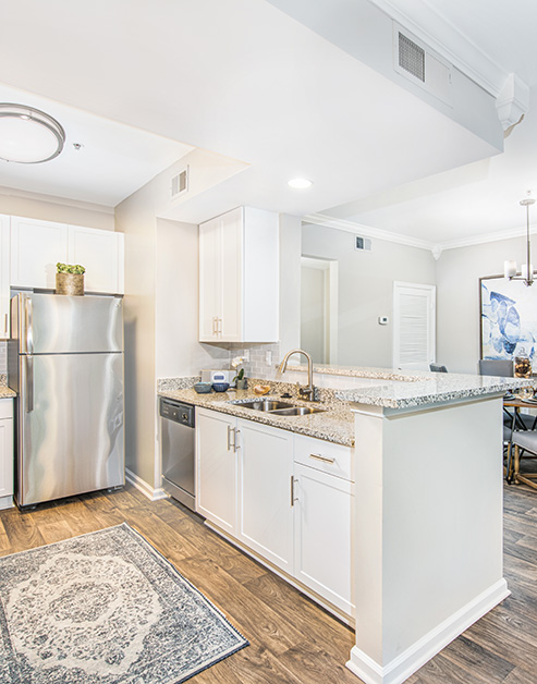 Modern kitchen with white cabinets, stainless steel appliances and granite countertops with wood floors next to living area at MAA Riverside luxury apartments in Atlanta, GA
