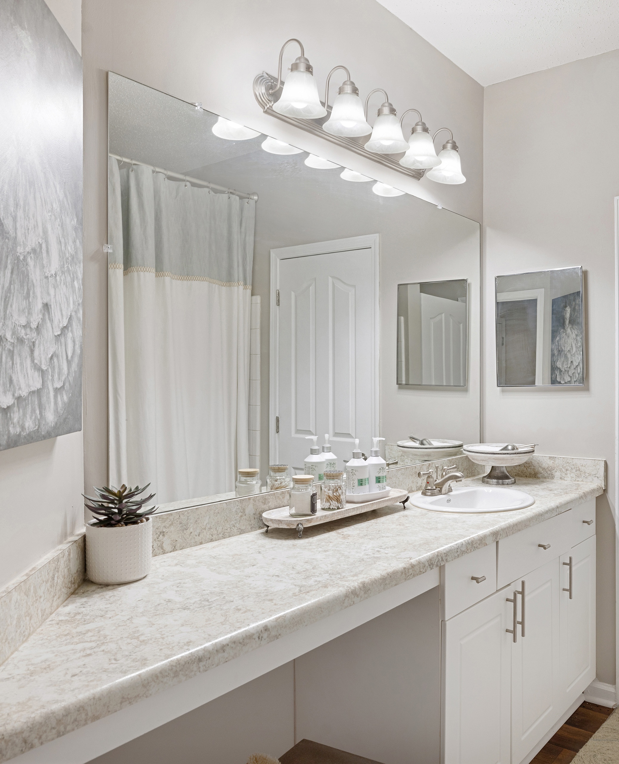 Modern bathroom with bright lighting above large vanity mirror and single sink at MAA Shiloh luxury apartments in Kennesaw, GA