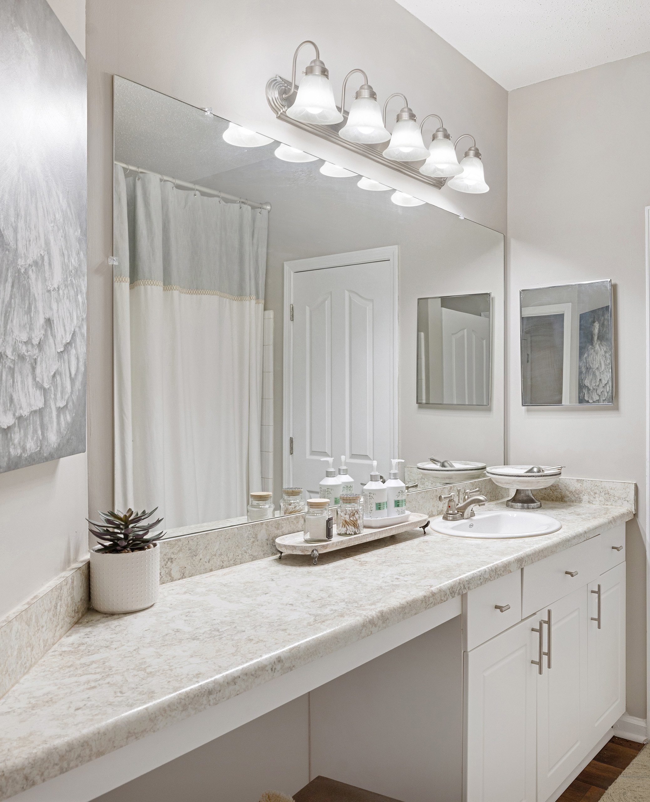 Modern bathroom with bright lighting above large vanity mirror and single sink at MAA Shiloh luxury apartments in Kennesaw, GA