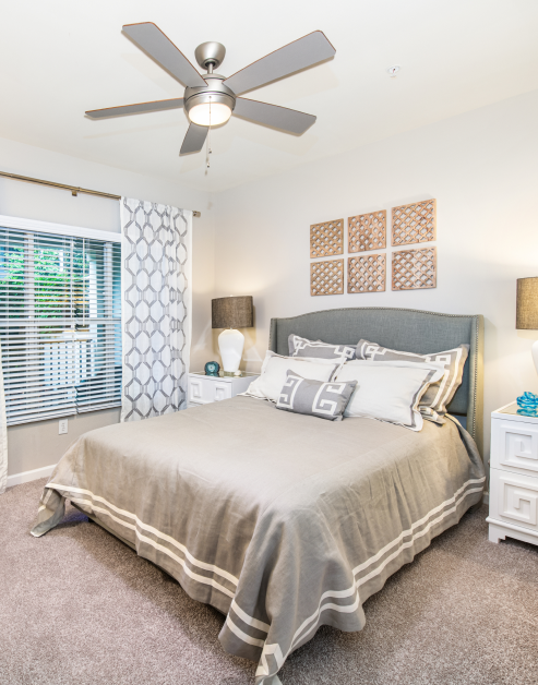 Model bedroom with neutral tone décor, ceiling fan and window curtains at MAA Spring luxury apartments in Smyrna, GA