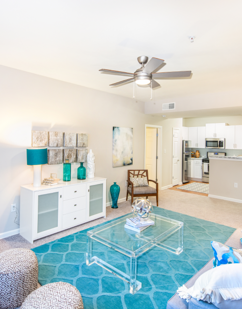 Model living room with blue area rug, ceiling fan and clear coffee table next to kitchen area at MAA Spring luxury apartments in Smyrna, GA