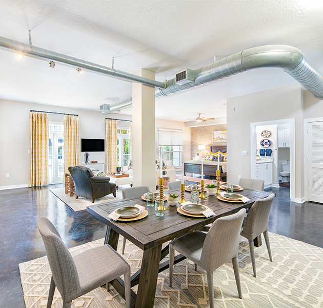 Apartment with an open floorplan living area with exposed ceiling duct system with a spacious dining area with wood dining table and chairs on concrete floors at MAA Stratford luxury apartments in Atlanta, GA