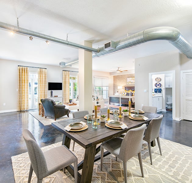 Apartment with an open floorplan living area with exposed ceiling duct system with a spacious dining area with wood dining table and chairs on concrete floors at MAA Stratford luxury apartments in Atlanta, GA